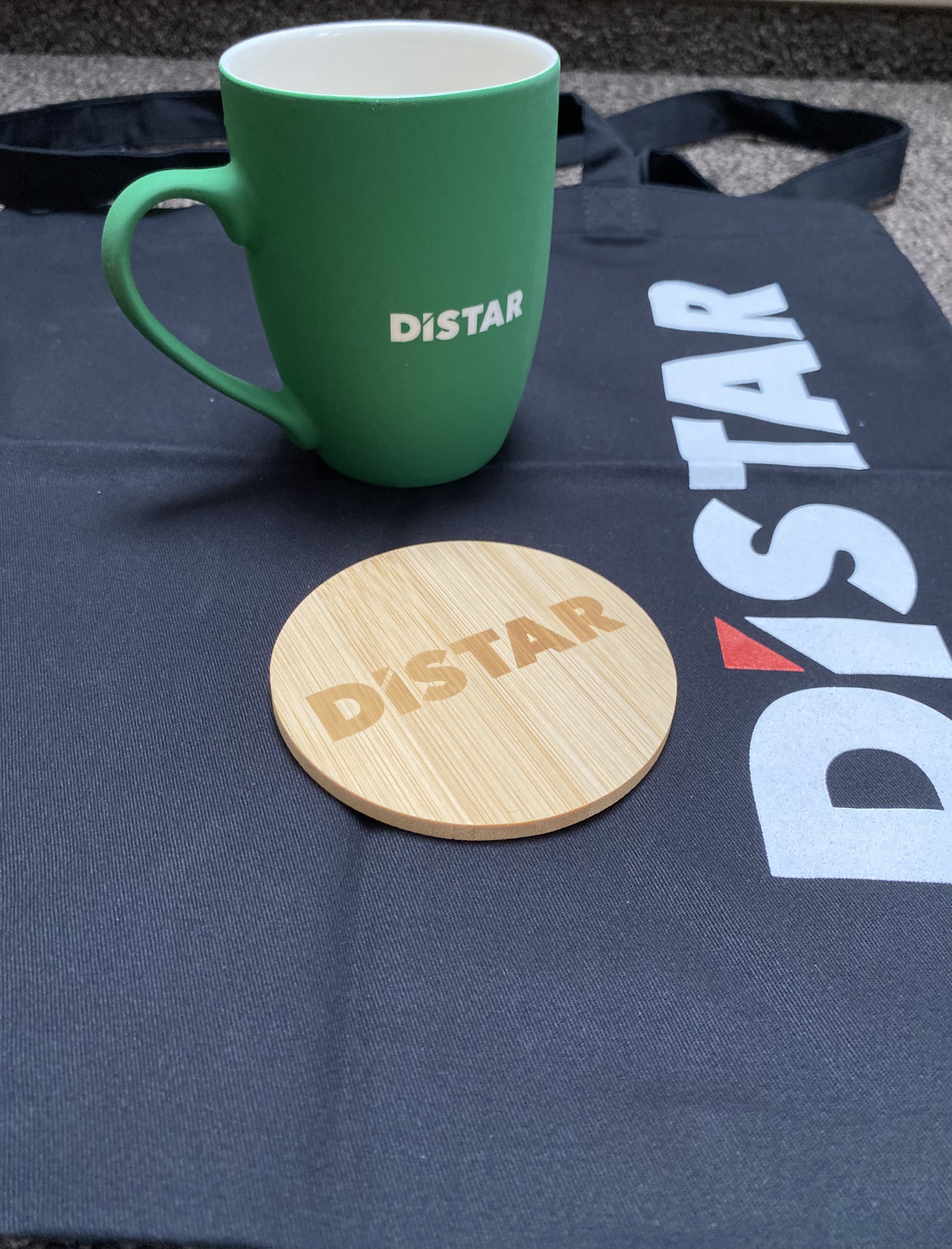 Zestaw gadżetów firmowych: kubek, drewniana podstawka, materiałowa torba.